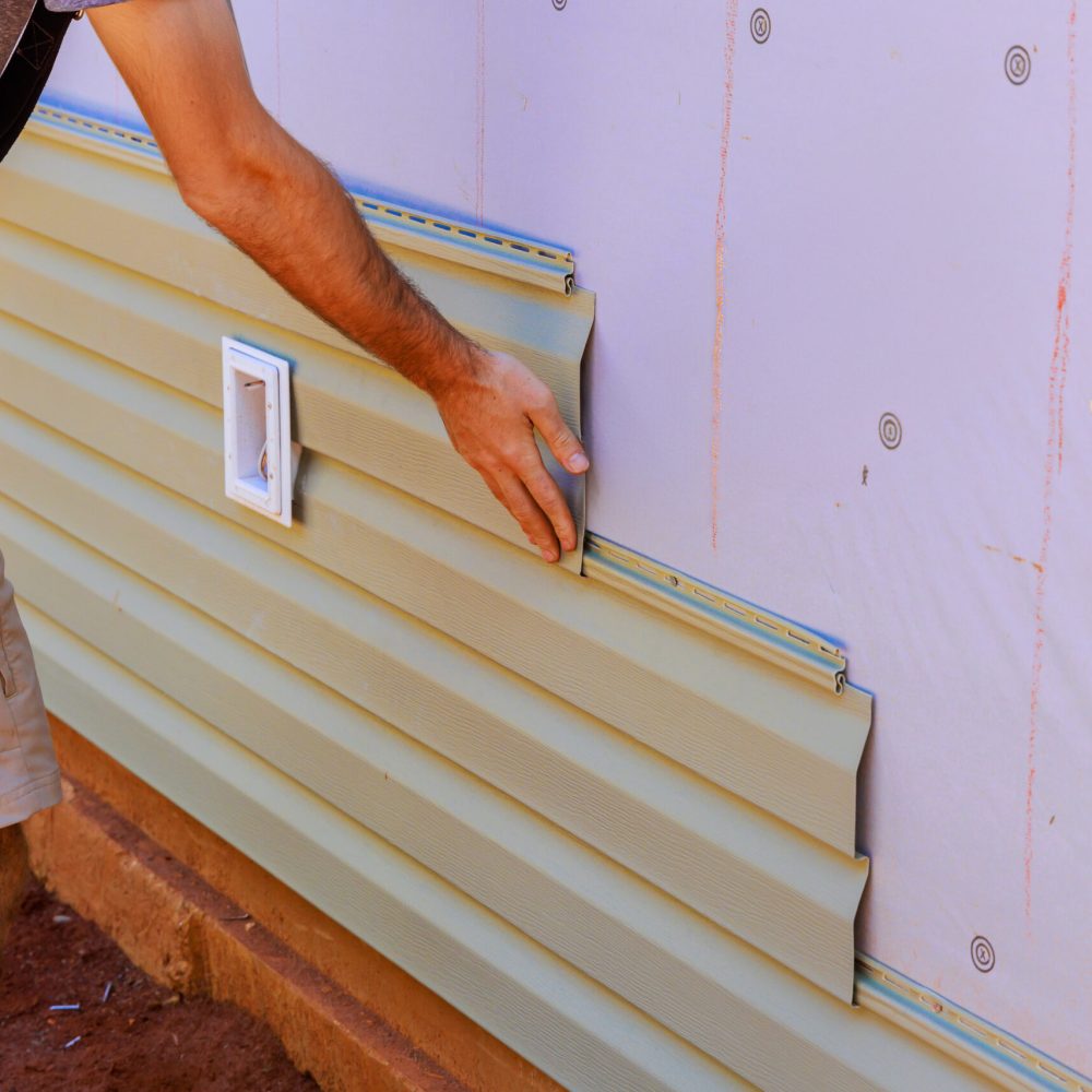 An employee installs vinyl plastic siding panels on wall facade of new residence